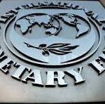 Metal plaque featuring a circular emblem with a globe and a winged symbol, surrounded by large raised lettering. The plaque appears silver on a dark background.