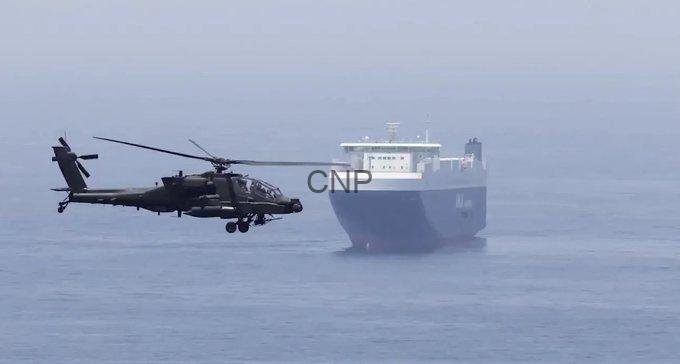 boats - Center News Network Military helicopter hovering near a large cargo ship at sea, as if preparing to deck or land or inspect the vessel (CNP watermark visible).