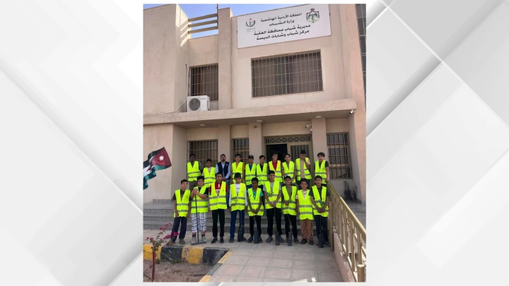Group of people in yellow safety vests posing in front of a beige building with an Arabic banner above the entrance.