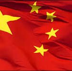Waving flag of China with a red field and five yellow stars, one large and four small, arranged in a pattern.