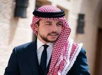 Portrait of a man in a dark suit and tie wearing a red-and-white keffiyeh headscarf, standing outdoors.