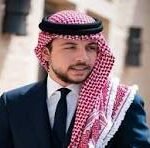 Portrait of a man in a navy suit with a white shirt, wearing a red-and-white keffiyeh scarf outdoors.