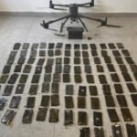Quadrotor drone on a tiled floor above dozens of black smartphones laid out in a grid as evidence.