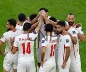 foot - Center News Network Group of football players in white jerseys celebrate in a huddle on a green pitch, raising their hands together in triumph.