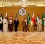 Group of dignitaries standing in a ceremonial hall with national flags and an emblem backdrop, posing for a formal photo.