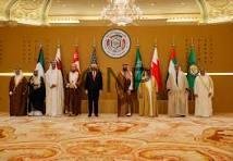 Group of dignitaries standing in a ceremonial hall with national flags and an emblem backdrop, posing for a formal photo.
