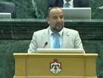Male official delivering a speech at a lectern in a formal legislative chamber.