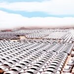 Thousands of white cars lined up in neat rows across a desert parking lot, stretching to the horizon.