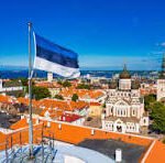 Israeli flag waving over a red-tiled rooftop, with a sunny historic city skyline in the distance.