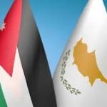 Two national flags fluttering side by side: Jordan (red triangle, black/white/green) and Cyprus (white with gold map and olive branches)
