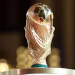 FIFA World Cup trophy gleaming gold on a pedestal with a blurred background, ready for presentation.