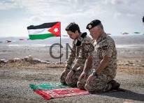 king wa - Center News Network Two soldiers kneeling on a rocky beach, paying respects to a Jordanian flag laid flat on the ground.