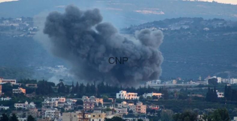 Massive dark smoke plume rising from a blast over a town, with houses in the foreground and hills in the background.