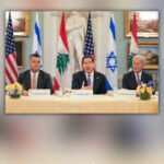 Three diplomats seated behind a conference table with microphones, flanked by US, Lebanese, Japanese, and Israeli flags in the background for a formal meeting.