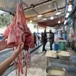 Person holding a slaughtered animal carcass in a busy meat market or processing area, with workers in the background.