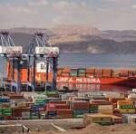 Port scene with colorful shipping containers and large cranes unloading a cargo ship on a calm sea, in the background left.