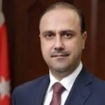 Portrait of a man in a navy suit and red tie, with a Turkish flag in the background.
