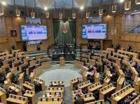 nww - Center News Network Parliament chamber with a central podium and semicircular rows of desks, flanked by large screens displaying information.