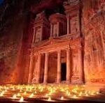 Night scene of a rock façade carved with 'GNP,' illuminated by warm candlelight along the ground.