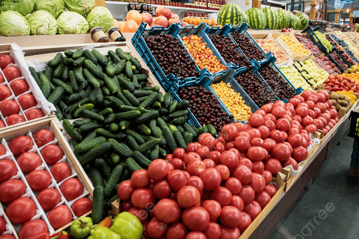 - Center News Network Fresh produce section with red tomatoes in the foreground, cucumbers piled beside them, and blue crates of small fruits in the middle at a supermarket.