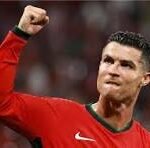 Soccer player in a red jersey raising a clenched fist in celebration on the field.