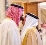 Two men in traditional Middle Eastern dress (thobes and ghutras) chatting indoors at an event.