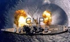 Warship on the water with two explosions and flames on its deck, producing smoke.