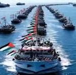 Flotilla of boats sailing in precise formation on a calm blue sea, lead ship flying an Indonesian flag.