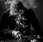 A person in a suit sits at a table in a dark, smoky scene with a skull in front of them.