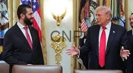 Two men in suits at a formal press event with American flags and a gold emblem in the background; one man gestures with open hands.