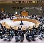 Delegates from many nations sit around a large circular conference table in a formal assembly hall, viewed from above.