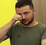 Man in a green t-shirt talking on a mobile phone with a yellow backdrop behind him.