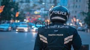 - Center News Network Traffic police officer seen from behind wearing a helmet and vest labeled 'Police' and 'Traffic Police' on a busy city street with flashing emergency lights in the distance