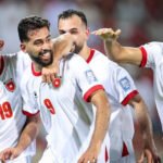 Jordanian national football team players celebrate a goal on the field, smiling and embracing each other.