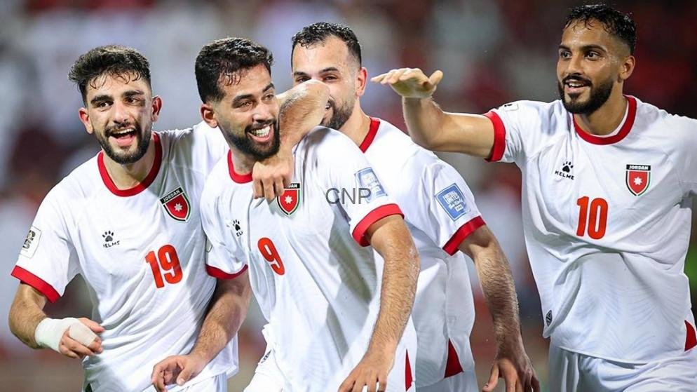 Jordanian national football team players celebrate a goal on the field, smiling and embracing each other.