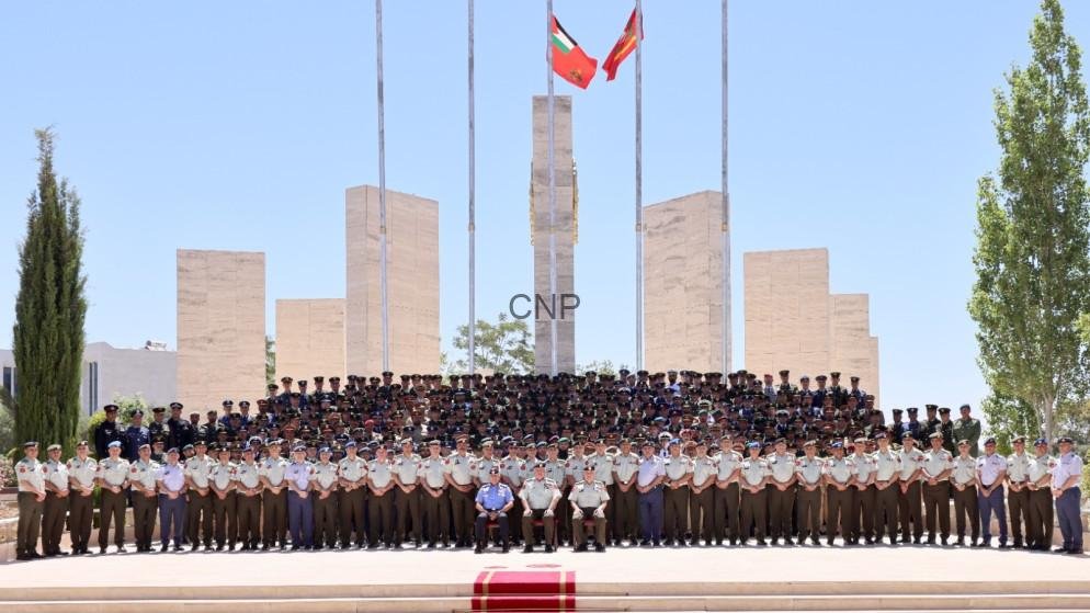 TAKH - Center News Network Large group of uniformed military personnel posing for a formal group photo in front of a stone monument with flags flying overhead.