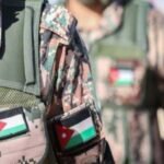 Close-up of two soldiers in camouflage vests with Jordan and Palestinian flag patches, in a desert setting.