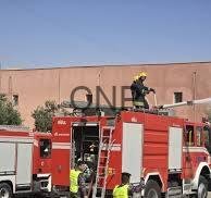 civdef - Center News Network Red fire truck with firefighters on the roof and a ladder extended toward a tan building under a clear blue sky, depicting an emergency response.