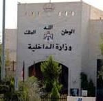 Front view of a beige building with Arabic signage and emblem on the facade, surrounded by trees; a black-and-white portrait poster appears on the right side.