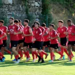 Group of young soccer players in red uniforms running on a sunny grass field during training.