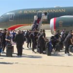 Passengers with rolling suitcases queue to board a Royal Jordanian airplane on the sunny tarmac.