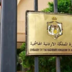 Brass plaque on a black gate reading 'Embassy of the Hashemite Kingdom of Jordan' with the Jordanian coat of arms above the text (Arabic and English).