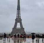 Eiffel Tower centered in view with crowds of people on a damp plaza under gray, cloudy skies.