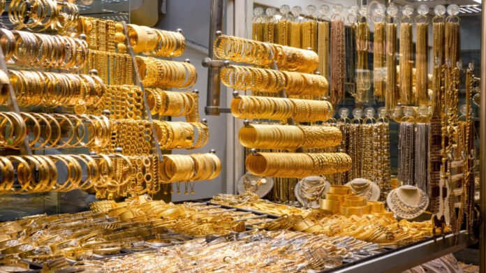 Gold jewelry display with stacked bracelets, bangles, and necklaces in a shop window.