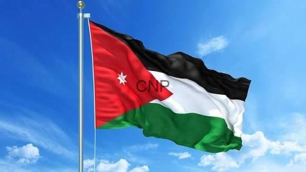 images 15 - Center News Network Jordanian flag fluttering on a flagpole against a bright blue sky, featuring a red triangle with a white star.