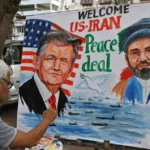 Street artist painting a large outdoor mural promoting a US–Iran peace deal, with two portrait figures and the words 'Peace deal' above water scene.