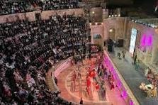 jarash - Center News Network Indoor arena with a circular performance pit and tiered audience seating, performers in red on a brightly lit stage surrounded by spectators.