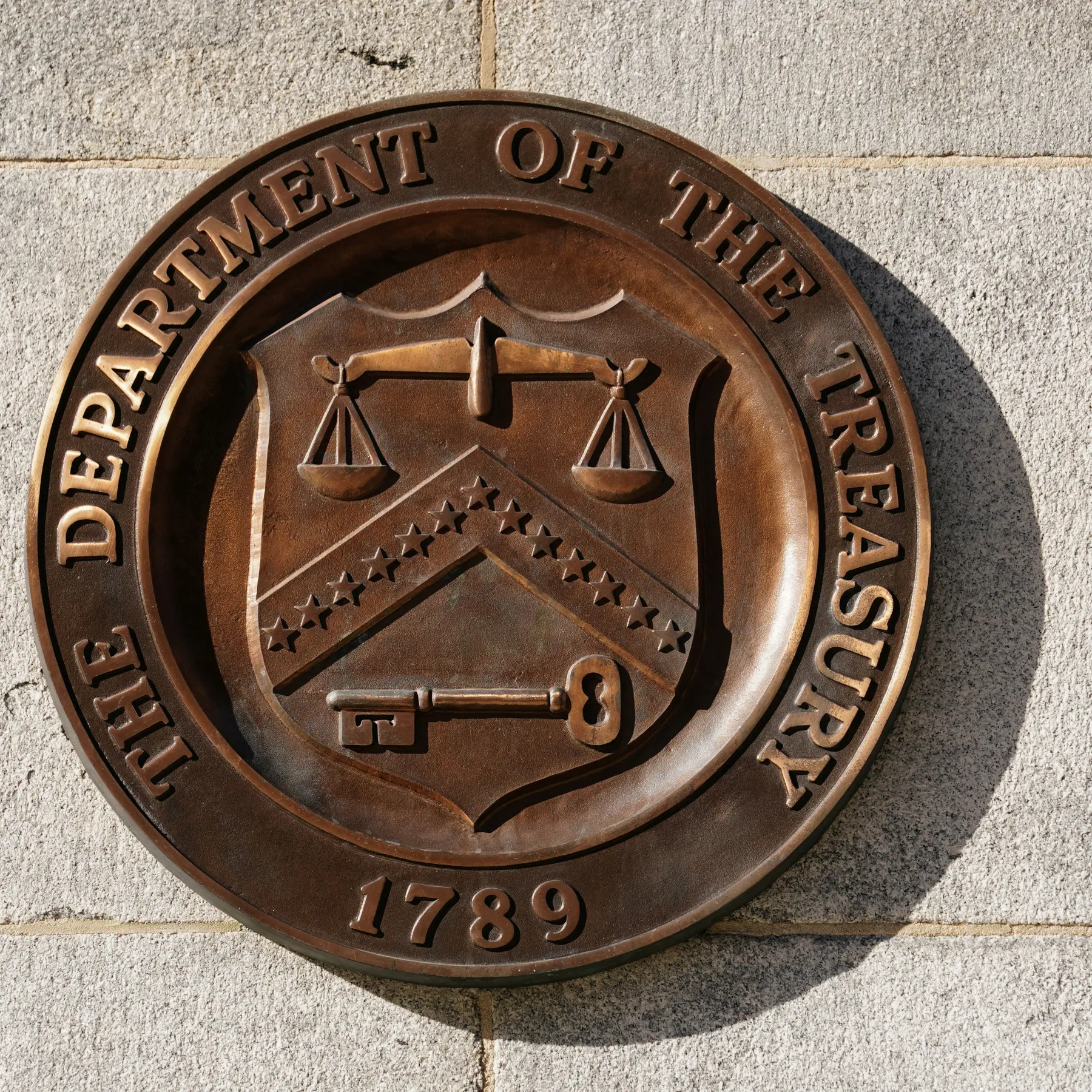 Bronze seal of the Department of the Treasury attached to a stone surface, showing scales and emblem, with 1789 at the bottom.
