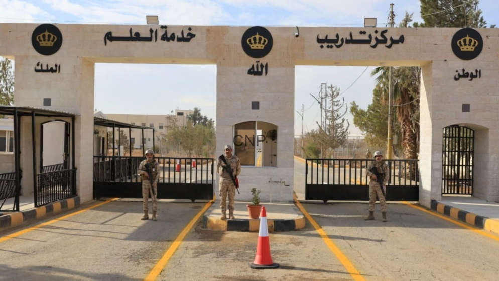 khed - Center News Network Border checkpoint entrance with three arches, armed soldiers standing guard, a small guardhouse between arches, yellow lane markings, and an orange traffic cone; Arabic signs and crown logos on the facade.
