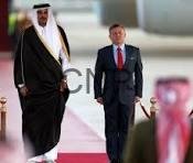 qatjo - Center News Network Two men walk down a red carpet together, one in traditional white-and-black robes with a head covering and the other in a dark suit and red tie, as onlookers photograph nearby.